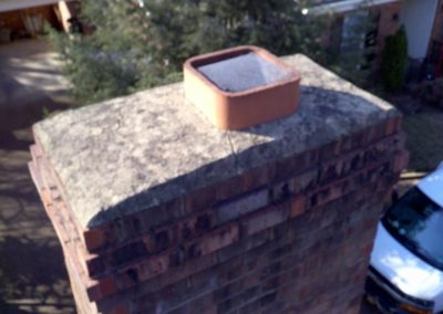 Exposed chimney flue with truck and homes in the background. The crown has a crack.