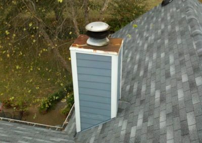 Rusted chimney chase cover with potted flowers and trees in background.