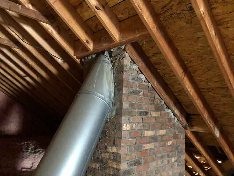 Safety inspection in the attic with flue going through brick and roof.
