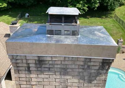 Chase Cover and cap on white brick chimney with trees and pool in the background.