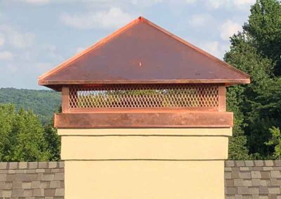 Custom copper chimney cap with roof and trees in background.
