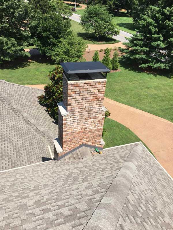 Black chimney cap on top of brick chimney with steps on the sides.