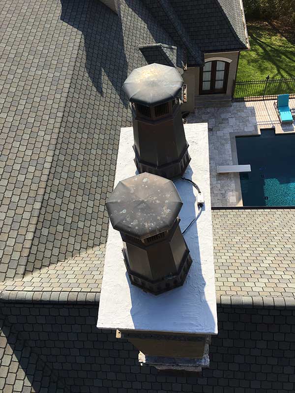 Double black chimney caps on roof with swimming pool and chair in background.