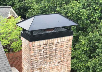 Custom black chimney Cap with trees in the background.