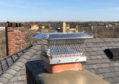 Stainless steel chimney cap with city in the background.