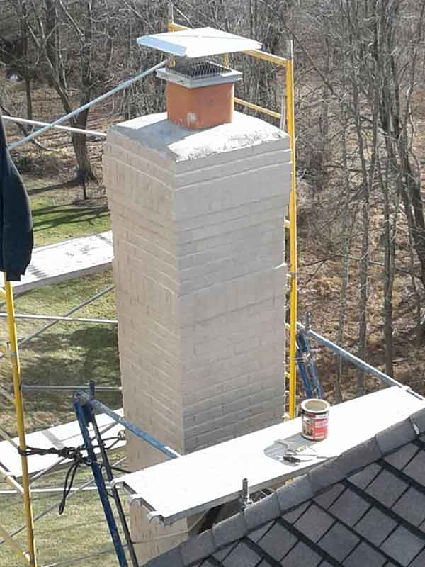 Chimney rebuild - cap with cage, terra cotta flue, white crown and chimney with scaffolding around.