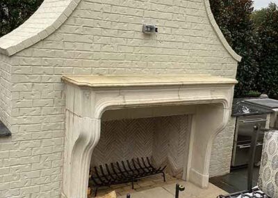 Beautiful cream colored outdoor wood fireplace situated in an outdoor kitchen.
