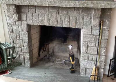 Stone fireplace with stone chinked mantel tools to the right and tv above.