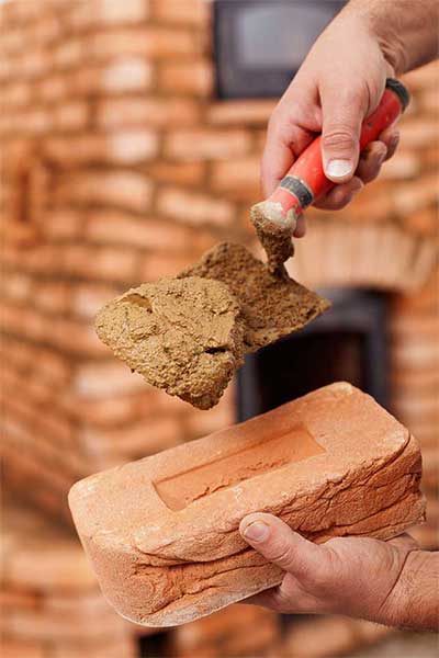 Hand putting mortar on brick with trowel.