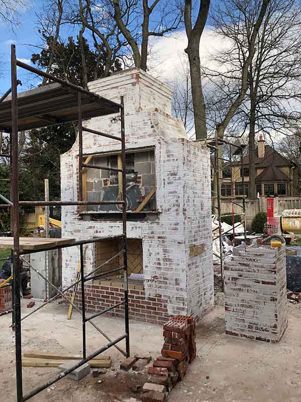 Outdoor chimney repair with scaffolding in front and large home in the back.