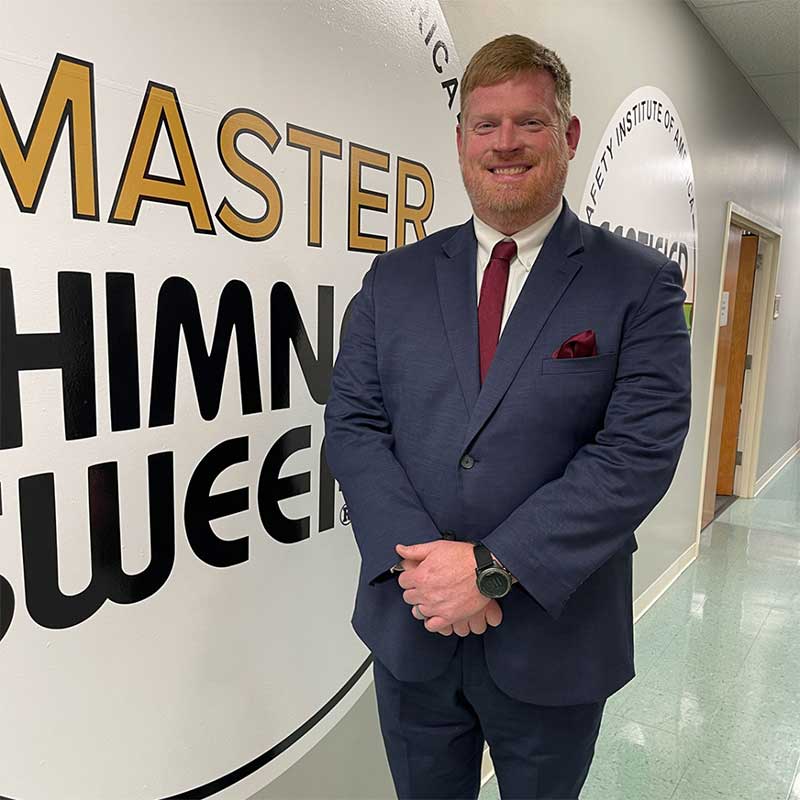 Tommy Nelms - Owner dressed in suit in front of Master Chimney Sweep sign.