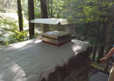 Hand holding sprayer waterproofing the chimney with woods in the background.